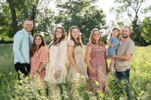 Extended family of seven standing in wildflower field 