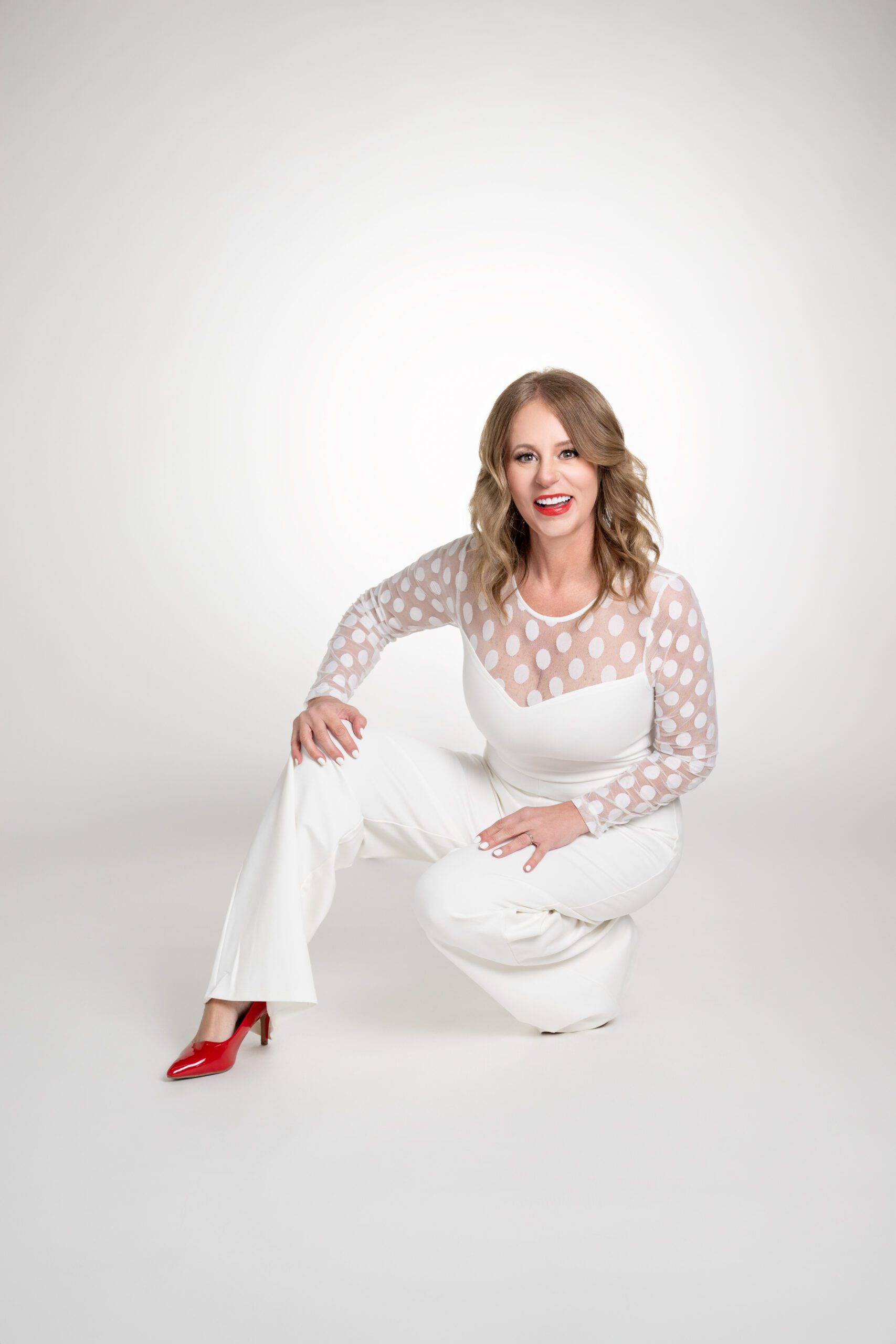 Business women crouching in front of white background with red shoes.