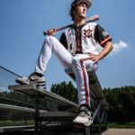 High school senior boy with baseball bat and uniform setting on brench